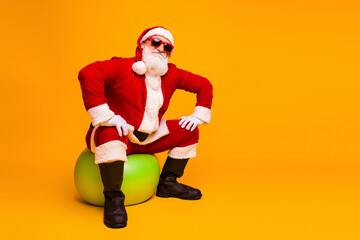 Santa in red costume sitting on a green ball with bright orange background perfect for Christmas campaigns and festive advertising