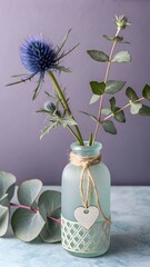 Single blue thistle flower in a decorative glass vase with eucalyptus leaves