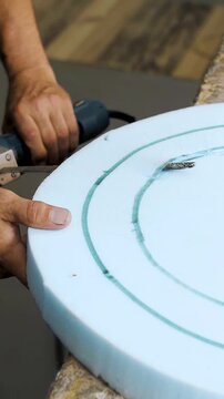 Vertical video. Close-up of a man's hands using a power tool to cut foam paralon for sofa production at a furniture factory. Close-up, slow motion.