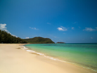 Peaceful tropical panorama sea beach with gentle waves rolling onto golden sand under bright blue sky with fluffy white clouds. relaxing summer scene perfect scene for travel holliday and nature lover