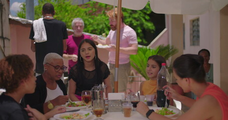 Family and friends gathered at a backyard table, enjoying food and drinks, casual lunch setting with sunny weather and relaxed bonding moments