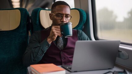 Concentrated african american businessman working on his laptop and drinking coffee while traveling by train, multitasking and staying connected with technology during his daily commute - Powered by Adobe