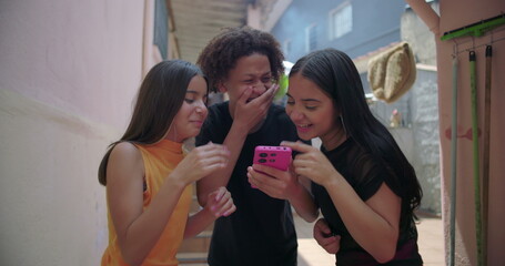 Teenagers gathered around a smartphone in suburban alleyway, sharing and enjoying social media...