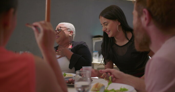 Group of friends laughing and enjoying a cheerful moment together at an outdoor dining table, showcasing diverse ethnicity and natural, authentic joy