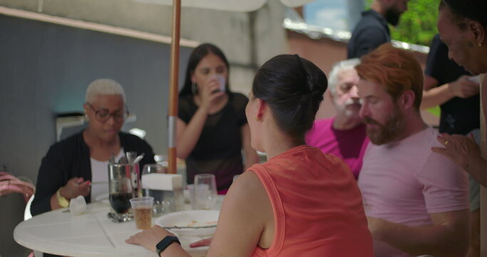 Group of friends and family seated at an outdoor table during a family BBQ lunch, sharing laughter and joyful moments in a warm and casual gathering - Powered by Adobe
