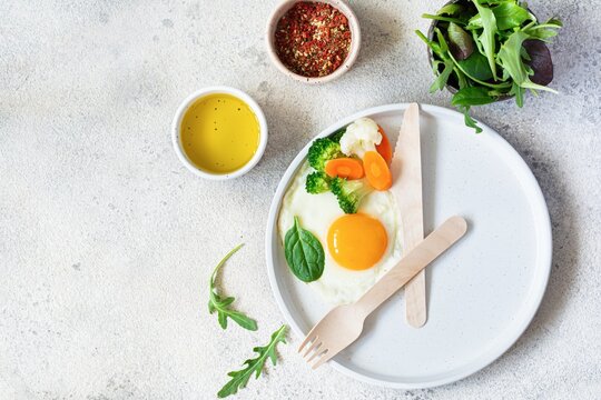 Healthy breakfast of fried egg and boiled vegetables with spinach on a light background. Healthy food concept, minimalism, top view.