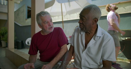 Obraz premium Two elderly friends sitting and conversing at a backyard barbecue, sharing meaningful dialogue and connection during a relaxed and casual outdoor gathering