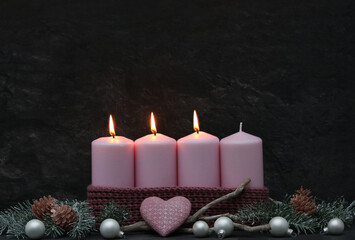 Decoration for the third Advent: Pink Advent candles with branches and Advent decorations against a dark background with space for text.