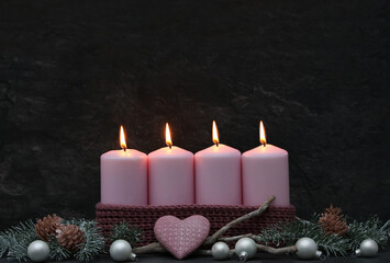 Decoration for the fourth Advent: Pink Advent candles with branches and Advent decorations against a dark background with space for text.