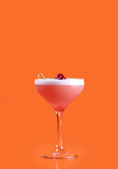 classic cosmopolitan drink in glass close-up isolated with foam and cherry garnish on orange background