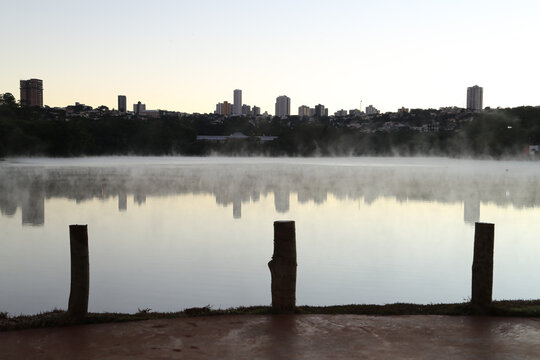 City skyline reflecting in calm lake water with morning mist