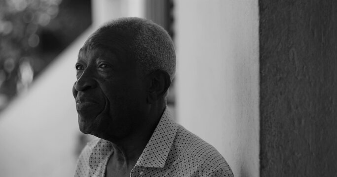 Elderly man looking sideways with a contemplative expression, leaning casually against a wall in an outdoor setting, exuding wisdom and introspection, black and white