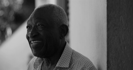 African American Elderly man smiling joyfully while leaning against a wall, exuding happiness, contentment, and warmth in an outdoor environment, black and white