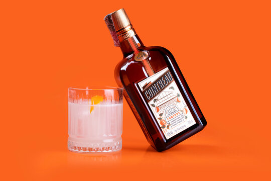 glass of refreshing drink with orange and cointreau bottle tilted on orange background