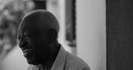 African American elderly man laughing joyfully while leaning against a wall, captured in black and white, exuding happiness, contentment, and emotional warmth