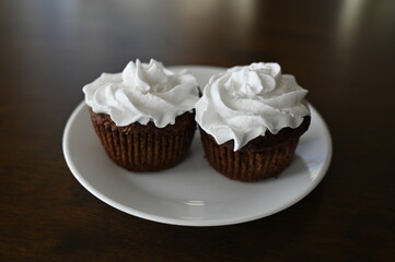 Two black bean and chocolate muffins with coconut whipped cream for a healthier snack on a small white plate and a brown tabletop. 