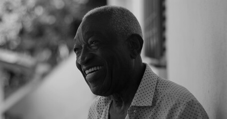 African American elderly man laughing joyfully while leaning against a wall, captured in black and...