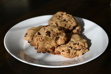 Homemade chocolate chips and walnut cookies on a white plate on brown table, sweet and warm for a morning snack. 