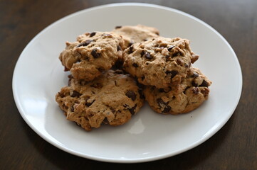 Homemade chocolate chips and walnut cookies on a white plate on brown table, sweet and warm for a morning snack. 