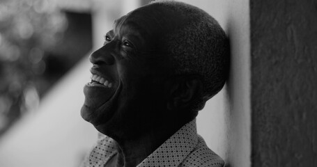 African American elderly man laughing while leaning against a wall, captured in black and white,...