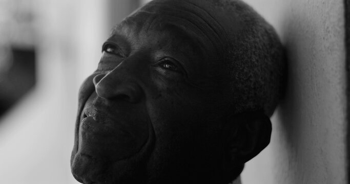 African American elderly man gazing upward with a serene expression, leaning against a wall in black and white, exuding calmness, wisdom, and introspection