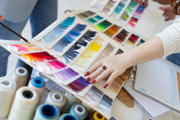 Hands choosing textile color shades in creative workspace. Collaboration, aesthetic decision, and teamwork in modern fashion design.