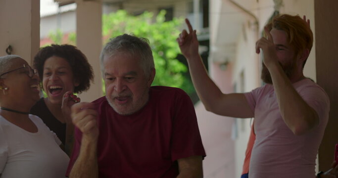 Elderly man dancing with joy in a group of diverse friends on porch, highlighting carefree energy and celebration in a lively outdoor social moment of bonding and fun