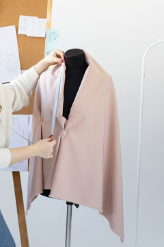 Tailor measuring fabric on black mannequin in fashion studio. Precision, craftsmanship, and garment creation process in professional atelier.