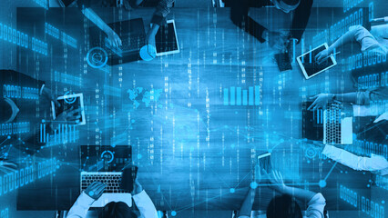 A top-down view of a modern collaborative workspace where diverse professionals use laptops and digital tools to analyze data trends and improve decision-making. Xenic