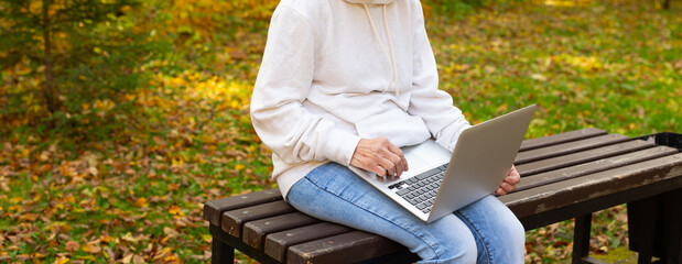 Close-up senior woman using laptop outdoors in autumn park. Banner. Digital literacy, mobility and freelance lifestyle for older adults