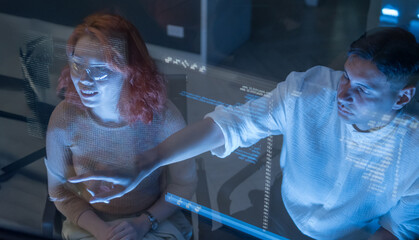 Man and woman team member collaborate on working digital project with code display on transparent screen. image highlight modern teamwork, technology, and innovation digital workspace in dark room.