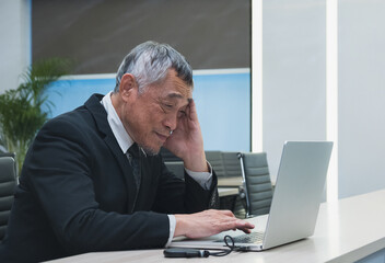 business man sit at desk with his hand on his head, looking stressed while analyzing business data on laptop screen. represent workplace pressure data analysis challenges, and business decision-making