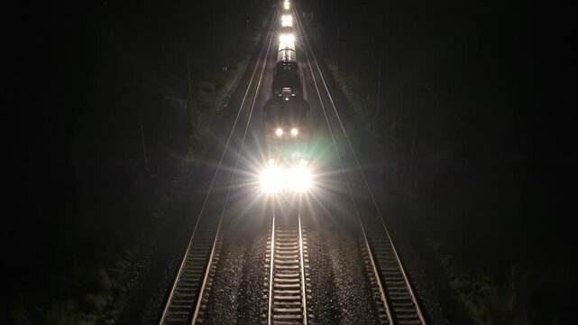 Train approaching at night on railway tracks with bright headlights.