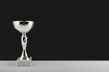 Silver winner cup on white table against black wall background.