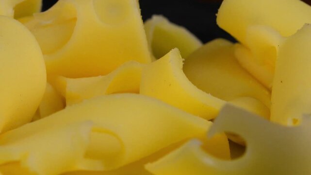 Slices of Emmental cheese on a black rotating background. Slices of Emmental cheese. Macro, close-up. Concept of veganism and healthy nutrition.