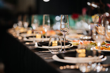 Closeup of elegant banquet table with glasses and black napkins in soft bokeh light