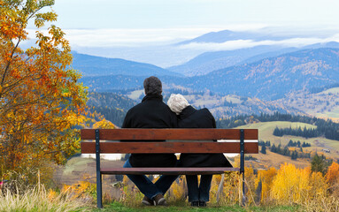Rear view of mature couple sitting on park bench overlooking valleys and mountains.