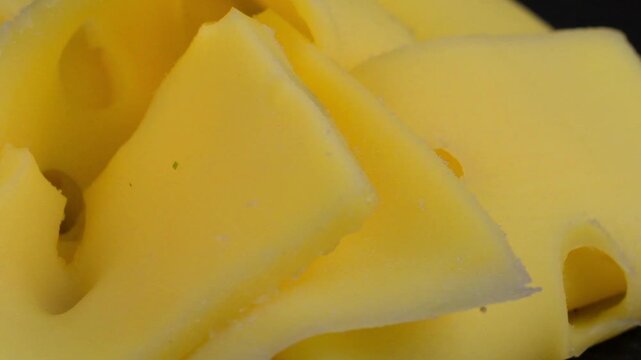 Slices of Emmental cheese on a black rotating background. Slices of Emmental cheese. Macro, close-up. Concept of veggies and healthy nutrition.