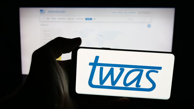 Stuttgart, Germany - 11-01-2025: Person holding mobile phone with logo of The World Academy of Sciences (TWAS) on screen in front of web page. Focus on phone display.