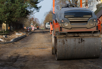 Fototapeta premium A heavy steamroller works on a dirt and gravel road, preparing the foundation for paving.