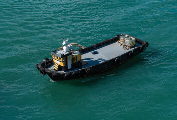 Obraz premium Small industrial tugboat or utility vessel with a yellow cabin, floating on turquoise water