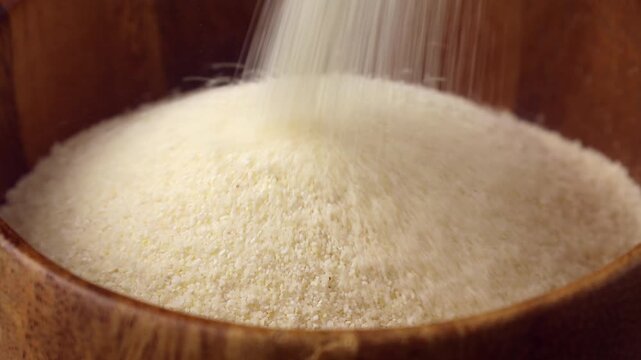Semolina falling down into the wooden bowl close up