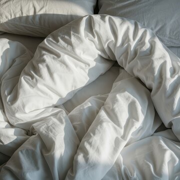 Unmade bed in the morning light showing crumpled white linen sheets and wrinkled blankets, suggesting recent sleep and relaxation ,hotel ,slumber ,lazy