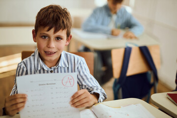 Happy schoolboy showing his A grade on a test at elementary school and looking at camera.	