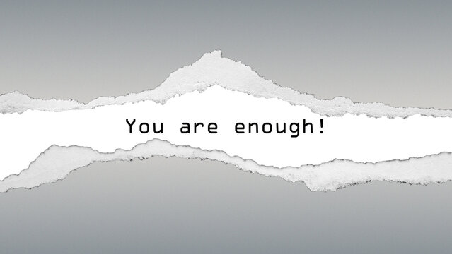 Inspirational quote “You are enough!” on torn paper texture with grey background. A positive message of self-worth and confidence.
