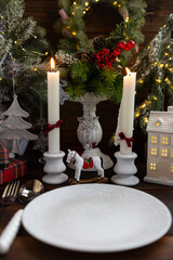 New Year's table setting with white candles and an elegant Christmas tree in the background. A festive and New Year's atmosphere.