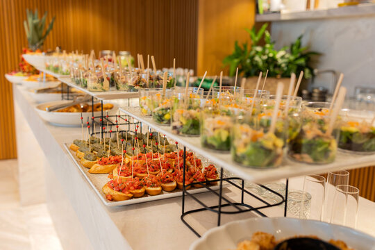 Elegant buffet table with assorted appetizers and salads. Modern catering buffet setup featuring assorted appetizers, bruschetta, and fresh salads in glass cups arranged neatly on a white table.

