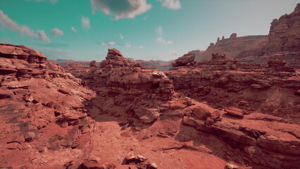 A breathtaking expanse of reddish brown rock formations stretches across the horizon, illuminated by the sun. Wispy clouds drift lazily in the blue sky, enhancing the serene atmosphere.