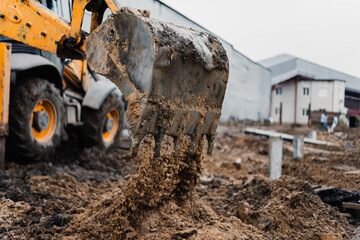 An excavator digs the ground for the foundation at the construction site. A yellow tractor pours earth out of the bucket. High quality photo © Rystemys