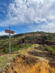 Mountain dirt trail with bike route sign under cloudy blue sky in spring landscape